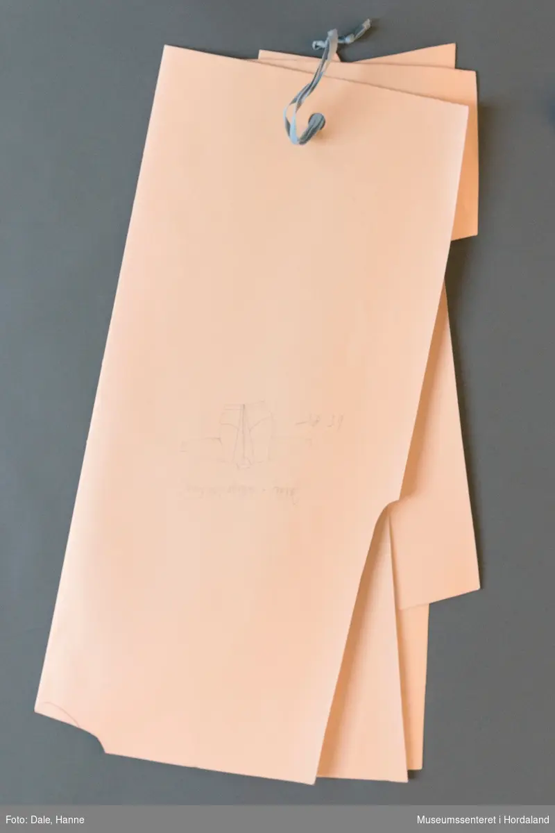 Mønsterskante i papp, brukt til å skjere ut ulike delar av plagg i klesproduksjon. Desse er til ei collegejakke med nummer 65.85. Skisse av plagget på skanten.