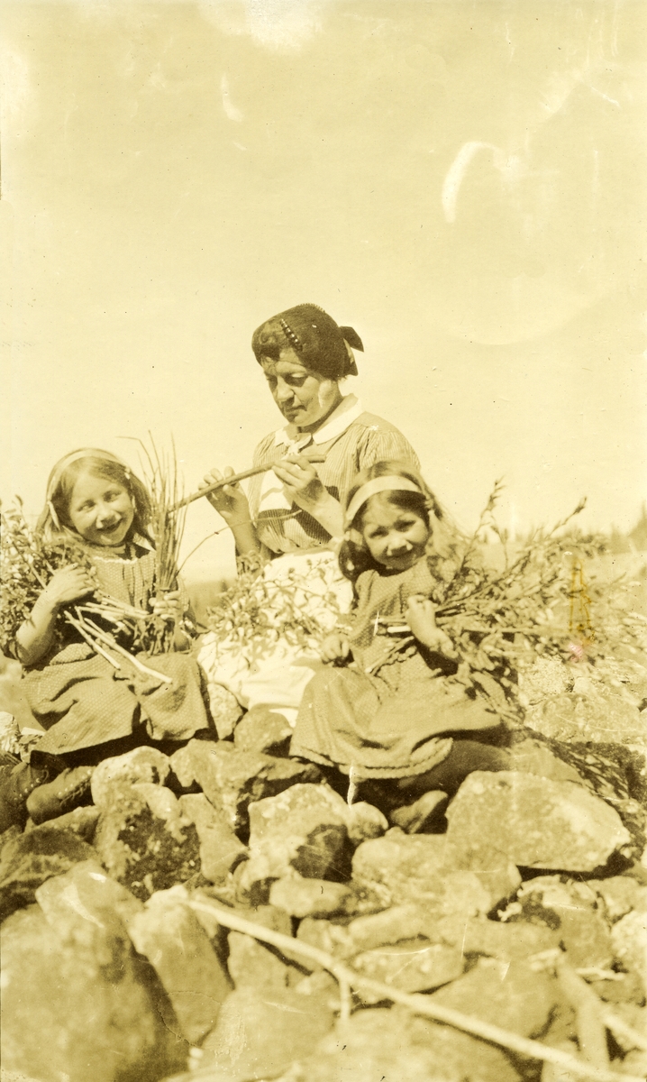Kvinne og to småpiker sittende i steinrøys i Galåsen med kvister/grasstrå i armene. Fra venstre: Målfrid Hauge f. Galaasen (1914), Oline Galaasen (1872 - 1944) og Ingebjørg Buflod f. Galaasen (1915 - 1999)