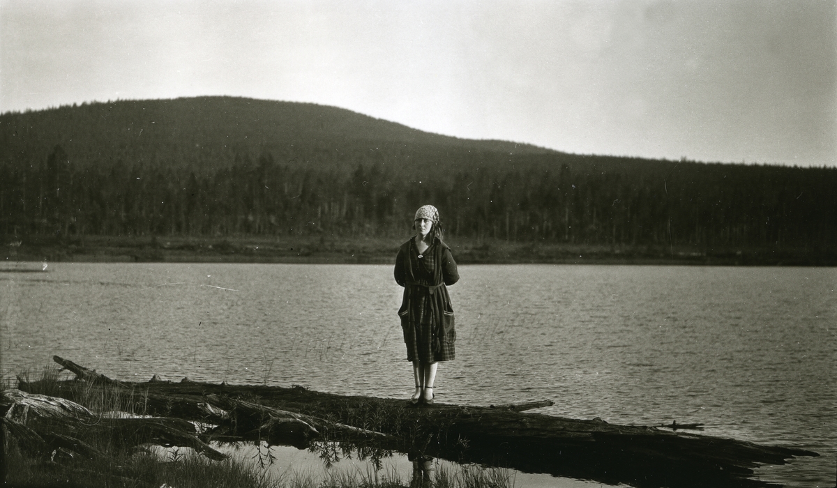 Kvinne stående på trestamme ved innsjø (Flersjøen)