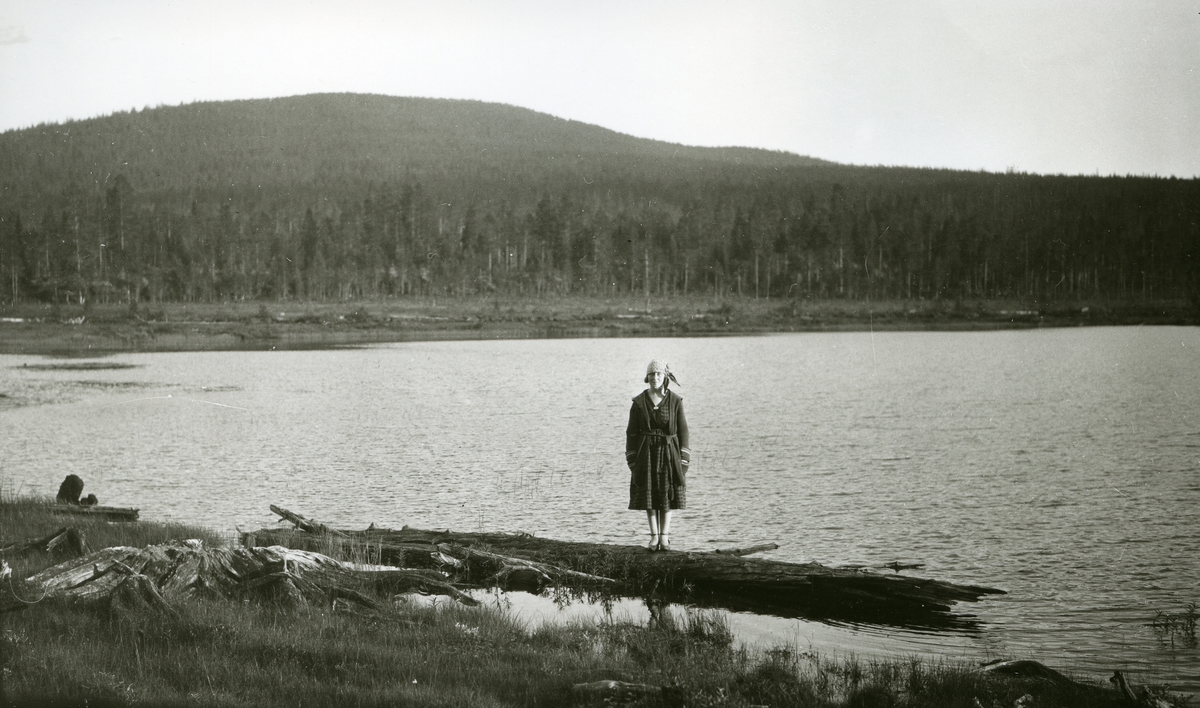 Kvinne stående på trestamme ved innsjø (Flersjøen).