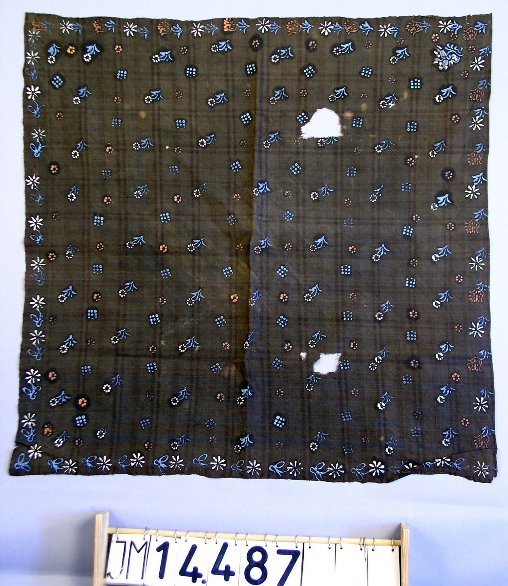 Huvudduk av mörkblått eller svart tuskaftvävt ylle med målat mönster av oljefärg föreställande små blommor i ljusblått, vitt och rosa.