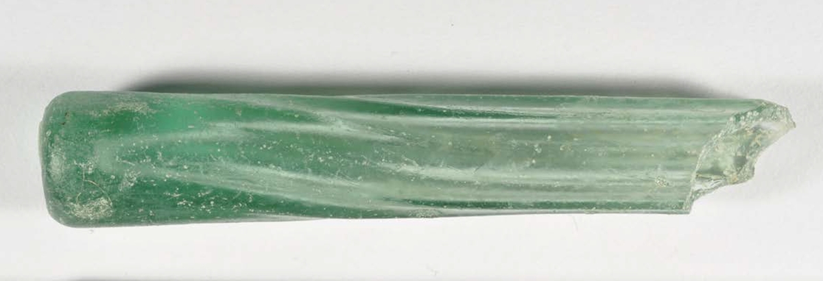 Flaska av glas. Näst intill komplett parfymflaska i ljusgrönt glas. Flaskan har ej varit stående, botten är något rundad, utan har förvarats liggande alternativt hängande. Datering 1600-tal.