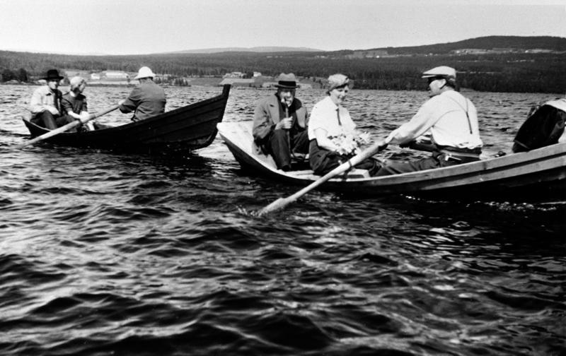 Svart-hvitt foto av to åfløyer (robåter) med folk oppi, utpå et relativt stille vann.