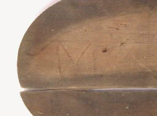 En oval botten till en svepask. Bottnen är i två delar. På bottnen finns spår efter åtta träpligg. På undersidan finns ett inristat M.