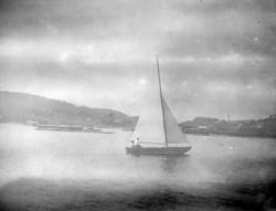 Seilbåt med to personer på vannet utenfor et kaiområde