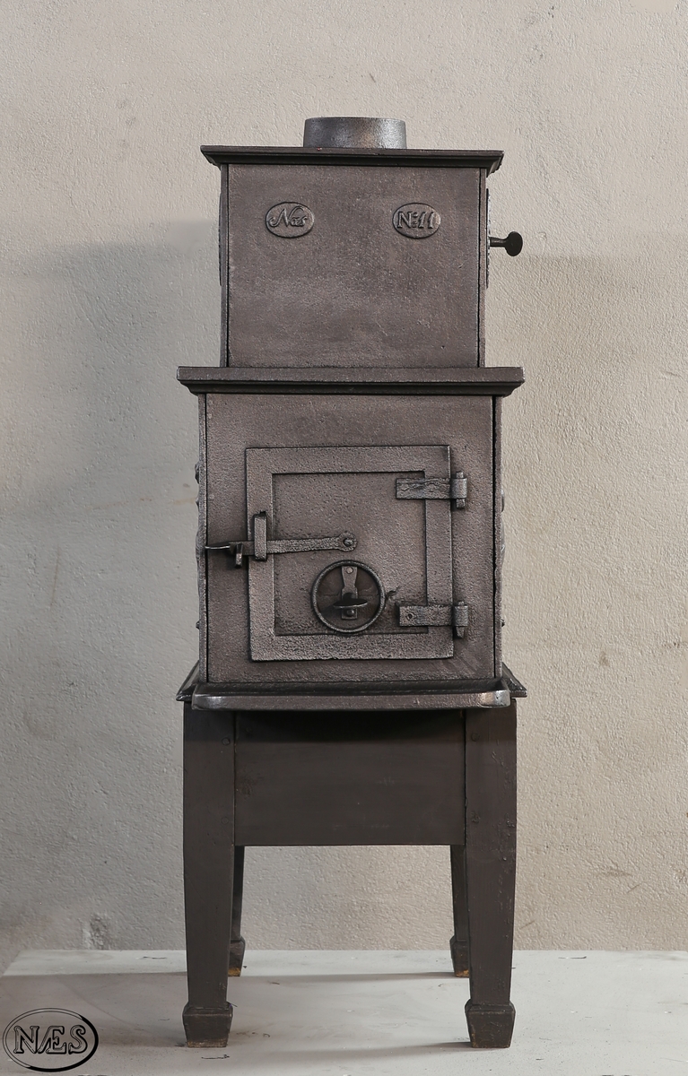 Kokeovn med to muser på enkel profillist. En fløytespillende og en dansende. Begge med draperier. Kokeanretning i topplaten til 1.etg. Ovnsdør på kortside. Rosett på begge sideplatene 2.etg. Den ene er løs og fungerer som ventil. Innskrift på frontplate og bakplate 2.etg. Røykuttak i toppen.