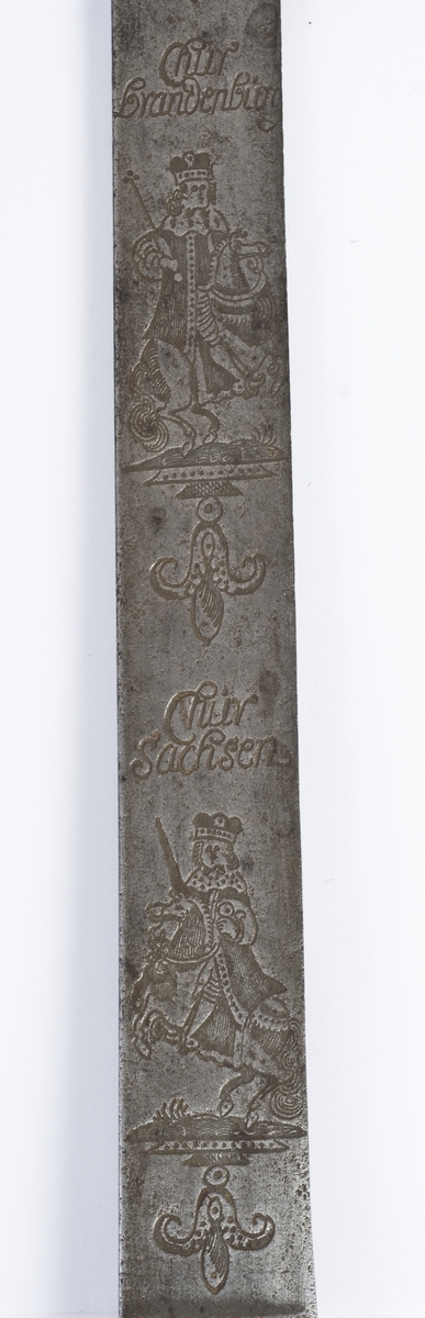 Messing feste fra en kårde. Rund fasettert knapp med nitteknapp.
Tregrep med snodd kobbertråde bevikling og bånd oppe og nede. Fremre parerstang brukket Bakre parerstang går over i håndbøylen, som er tappet inn i knappen.Parerplaten er fjernet, rektangulært baisstykke.
Rett enegget klinge med kileformet tverrsnitt og to smale ryggstillt blodrender.
Klingen har etset dekor med nanvgitte figurer og andre jaktscener.