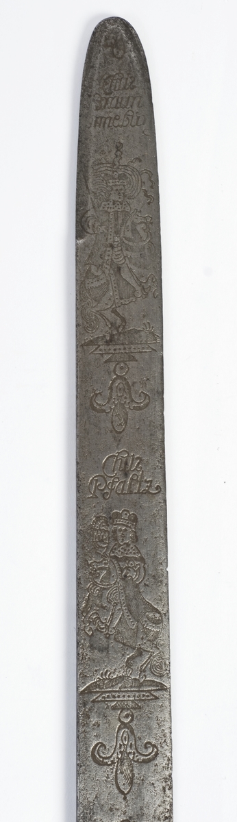 Messing feste fra en kårde. Rund fasettert knapp med nitteknapp.
Tregrep med snodd kobbertråde bevikling og bånd oppe og nede. Fremre parerstang brukket Bakre parerstang går over i håndbøylen, som er tappet inn i knappen.Parerplaten er fjernet, rektangulært baisstykke.
Rett enegget klinge med kileformet tverrsnitt og to smale ryggstillt blodrender.
Klingen har etset dekor med nanvgitte figurer og andre jaktscener.