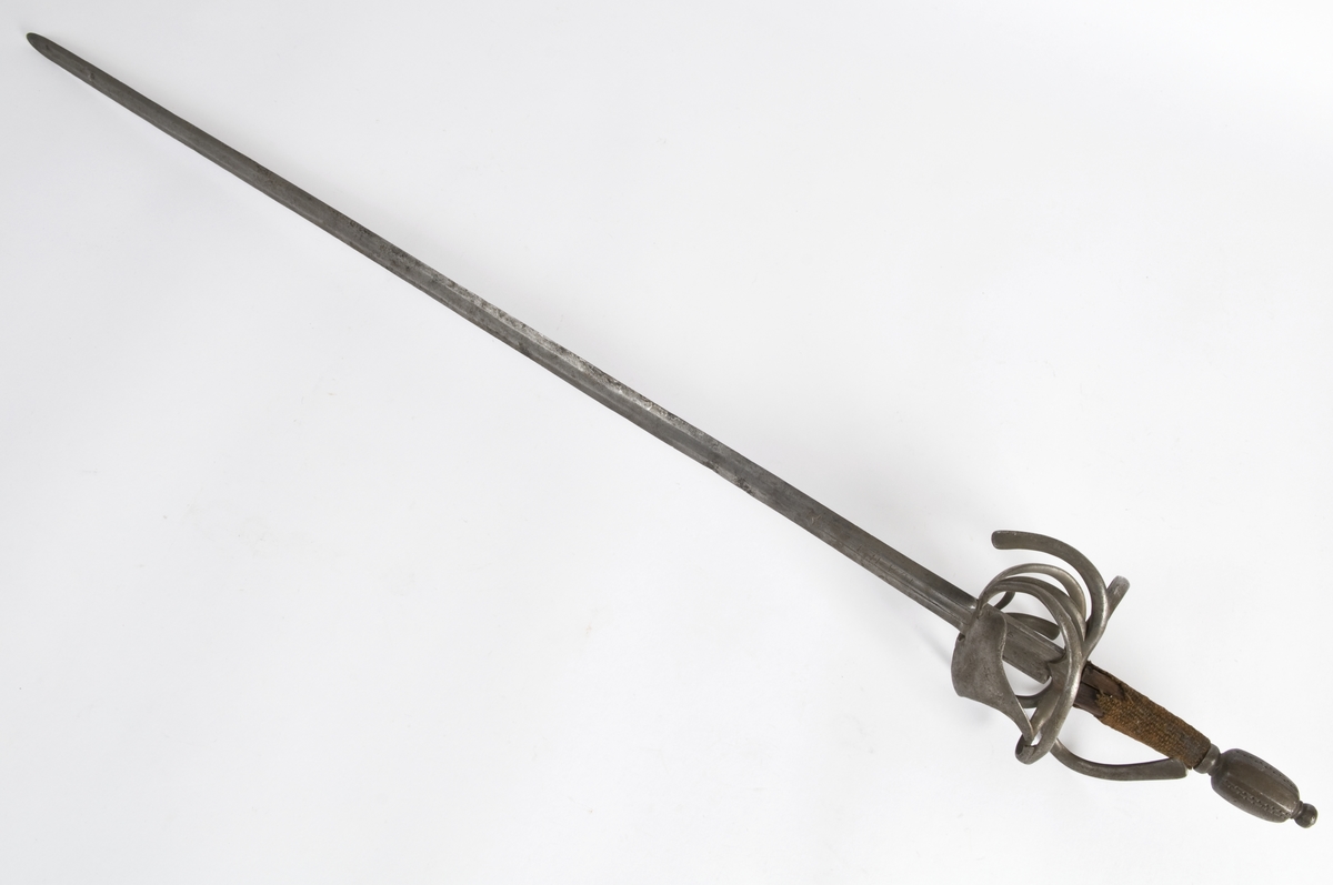 Plommeformet  8 kantet knapp. Tregrep.. Asymmetrisk feste med flate parerbøyler.  S formede parerstenger..Fremre parerstang går over i håndbøylen.Oppbøyet skjellformet parerplate på innsiden.
Tveegget, rett klinge med 6 kantet tverrsnitt  Kort blodrand merket IVAN