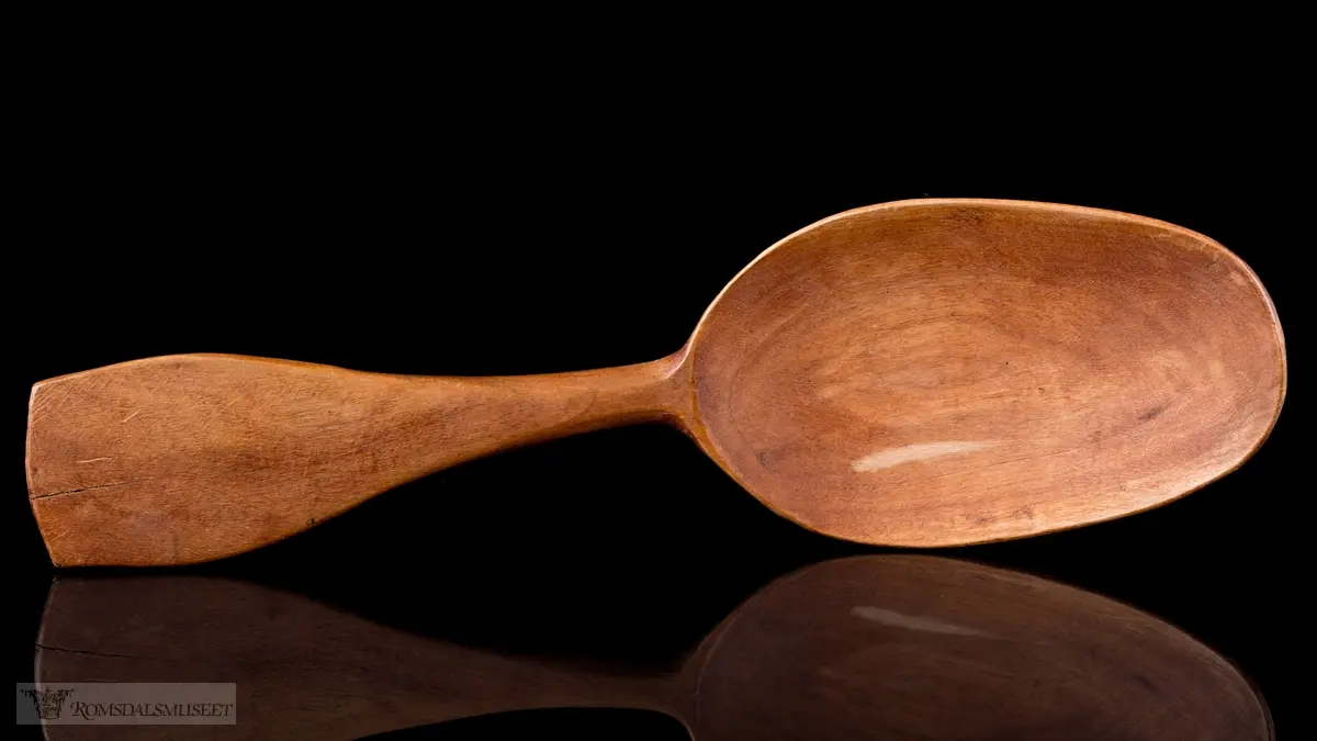 Enkelt formet og lakkert treskje uten dekor. Bredt flatt skaft og langt ovalt skjeblad.