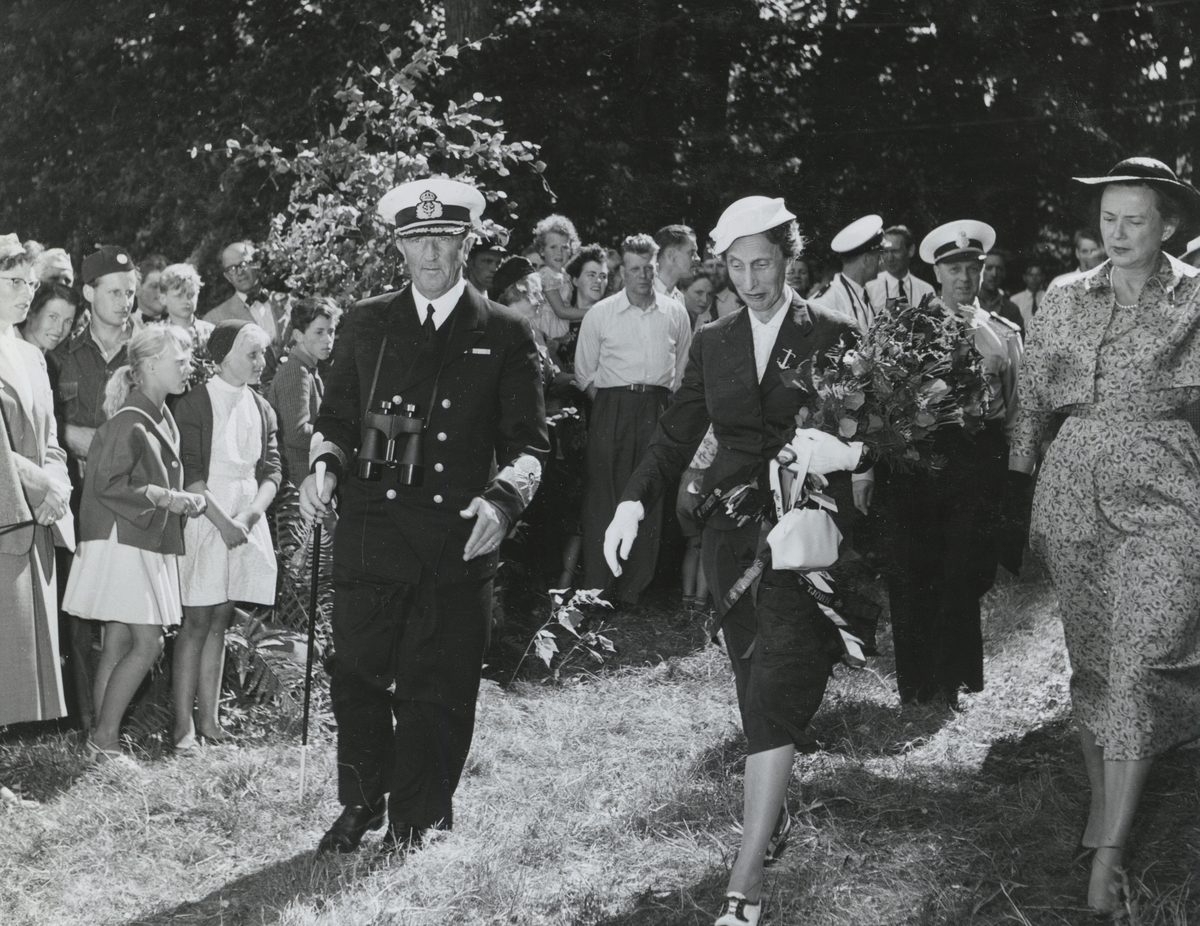 Konteramiral Samuelson går tillsammans med drottning Louise och en till kvinna över gräset längs en samling civila människor, bland annat barn. Detta är under Operation Kullen. Amiralen har en kikare runt halsen. Drottningen bär en bukett blommor och sin handväska.