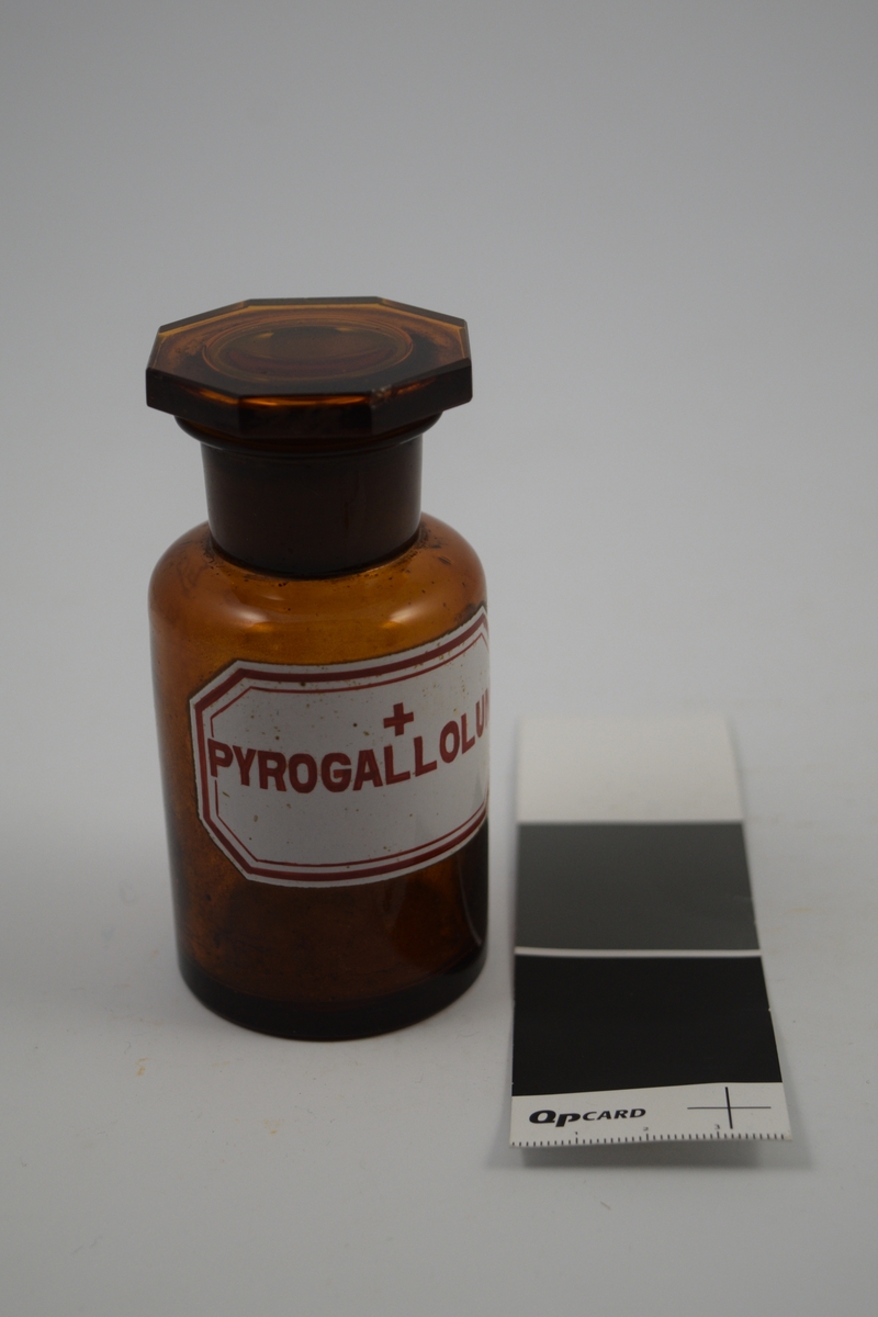 Glassflaske, brun med brun propp. Påført etikett; hvit med rød skrift. Ett rødt kors - betyr at innholdet er giftig. Pyrogallolum, "tretjære", ble brukt i salver mot eksem.