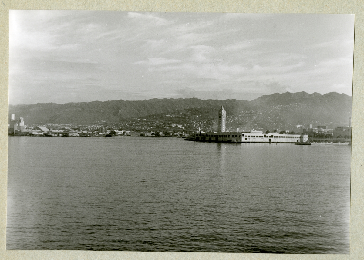 Bilden föreställer ett berglandskap. Längs med kustlinjen syns bebyggelse. Bilden är tagen under minfartyget Älvsnabbens långresa 1966-1967.