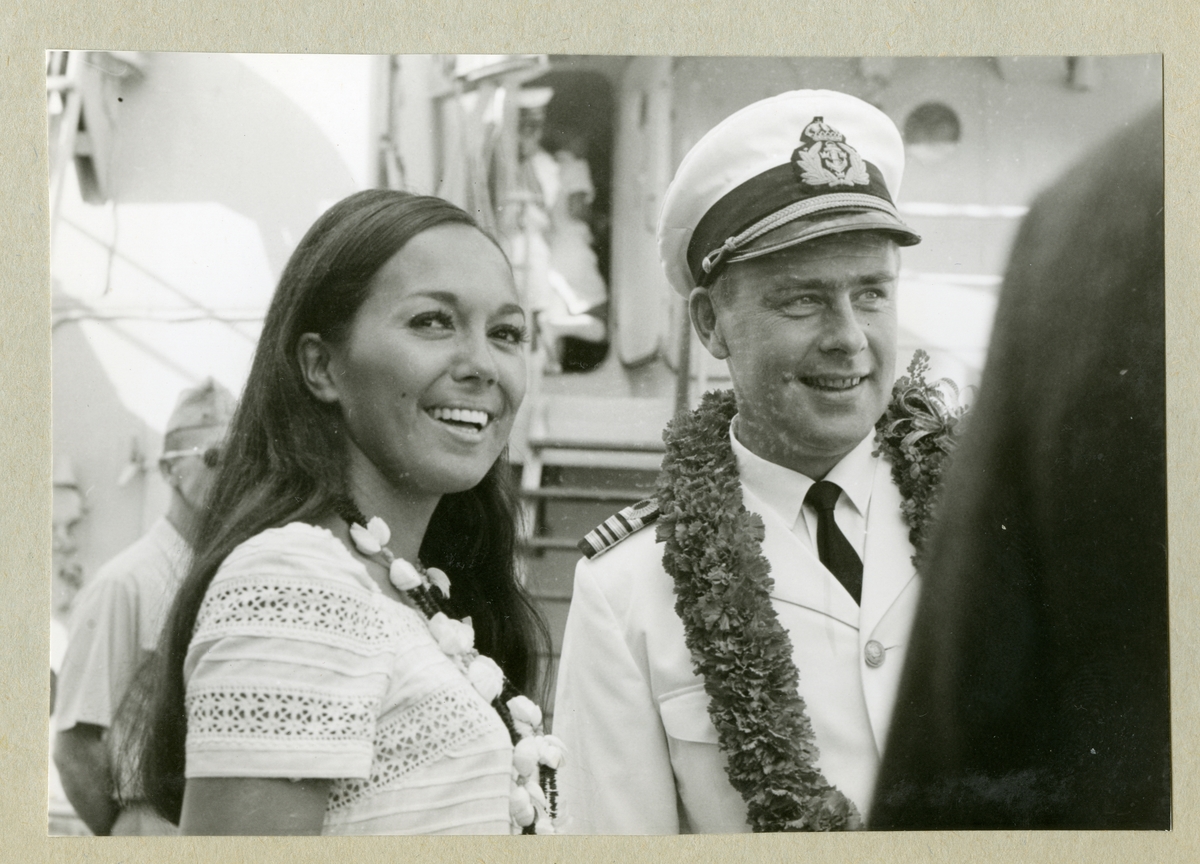 Bilden föreställer en kvinna och en besättningsman i vit uniform. Runt halsen är de utsmyckade med halsband. Bilden är tagen under minfartyget Älvsnabbens långresa 1966-1967.