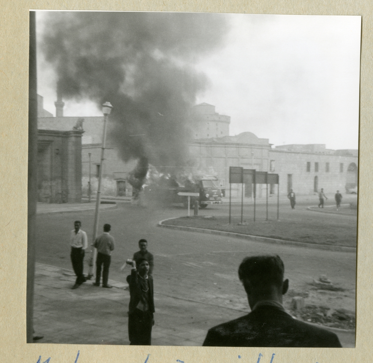 Bilden föreställer en buss, vilken det kommer kraftig rök ifrån. På bilden syns även byggader och människor i omgivningen. Bilden är tagen i samband med minfartyget Älvsnabbens långresa 1966-1967.