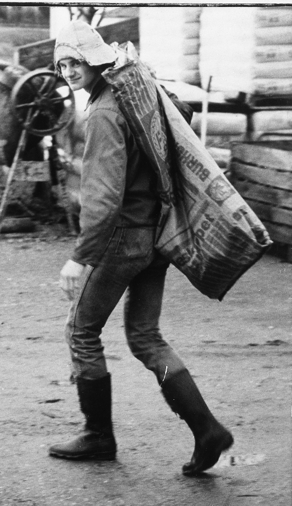 Gisle Høyland (29.6.1964 - ) i gardsromet på Børaholen på Ree, bnr. 94, ein lørdag ettermiddag. Når måkinga i hønsehuset er unnagjord må dei daude hønene berast bort - i papirsekken på ryggen.