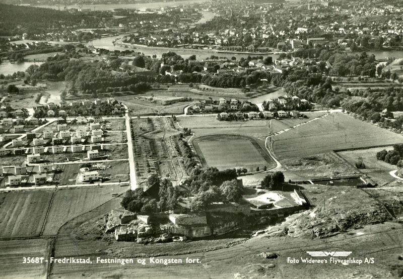 Fredrikstad. Østsiden. Gamlebyen i bakgrunnen. Vestsiden øverst i bildet. Kongstenområdet nærmest. Kongstenbanen. Den dekkede vei (t.v. for  banen). På omådet fra banen og mot høyre, ble idretts- og ustillingshallem oppført og innviet i 1971. Kongsten for (nærmest på bildet), oppført i 1680-årene på en ensom klippe, Galgeberget, som tidligere var rettested. Til venstre: nybygde bolighus i Kongsten haveby.