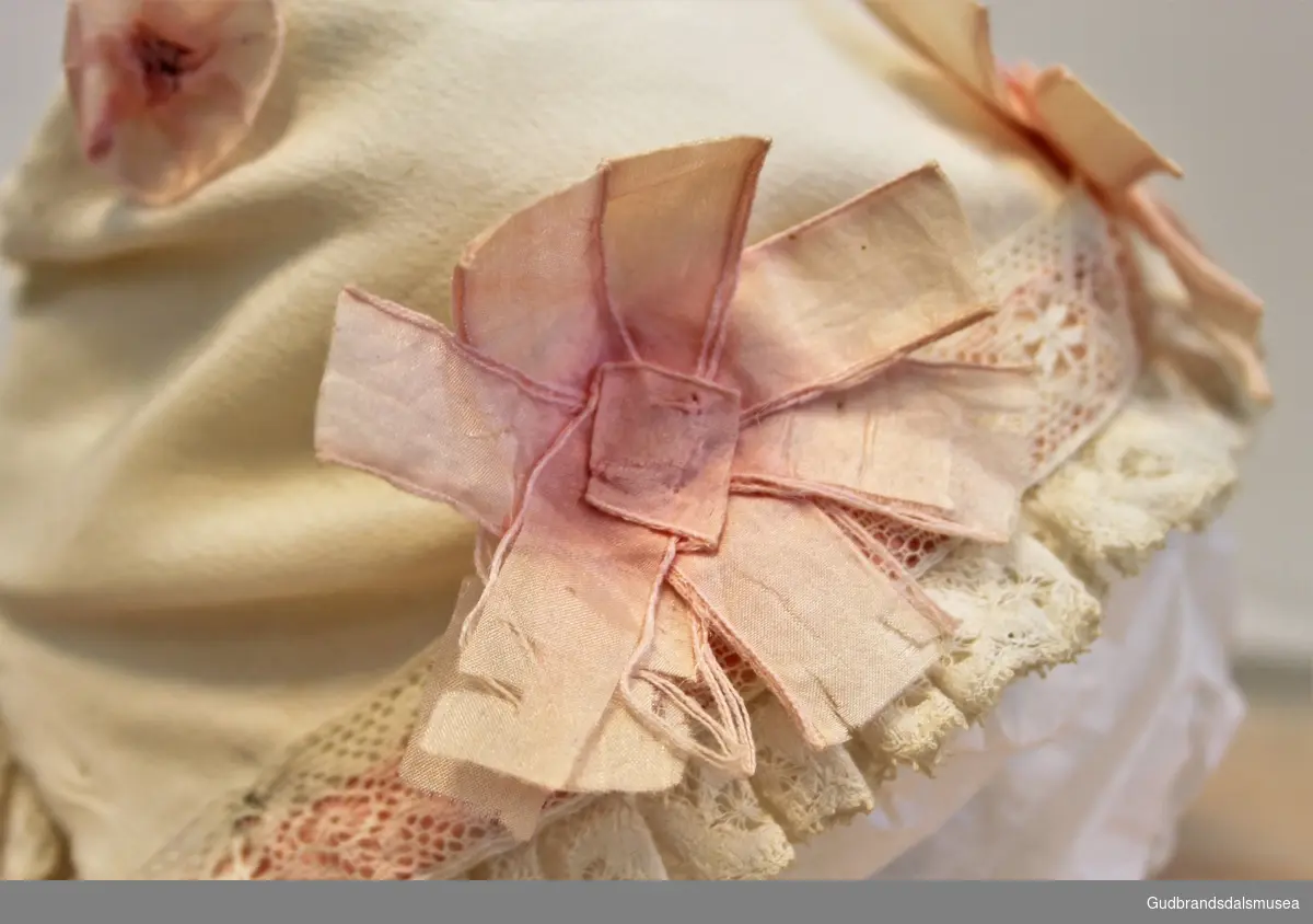 Hvit dåpslue i silkestoff, med engelskbrodert kant, påsydd fem rosa stjerner.