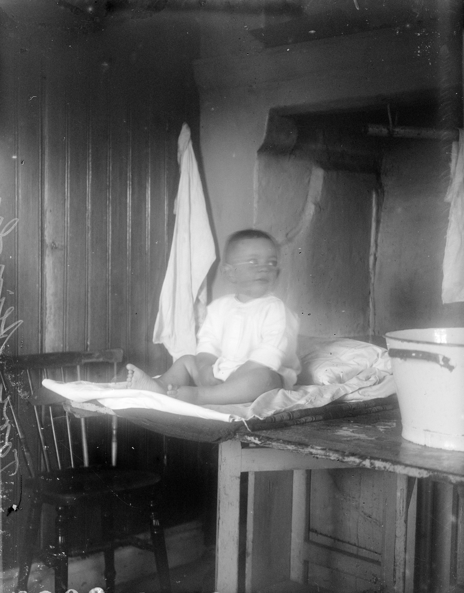 Tore Alinder sitter på bordet i köket, Sävasta, Altuna socken, Uppland 1925