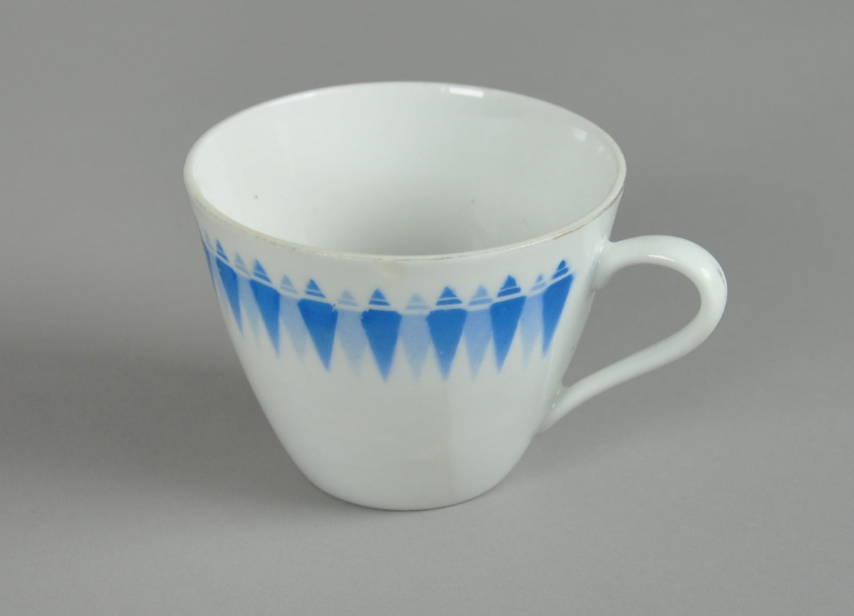 Kopp til servise, av glassert keramikk. På koppen er det malt dekor med motiv av blå romber på rekke.