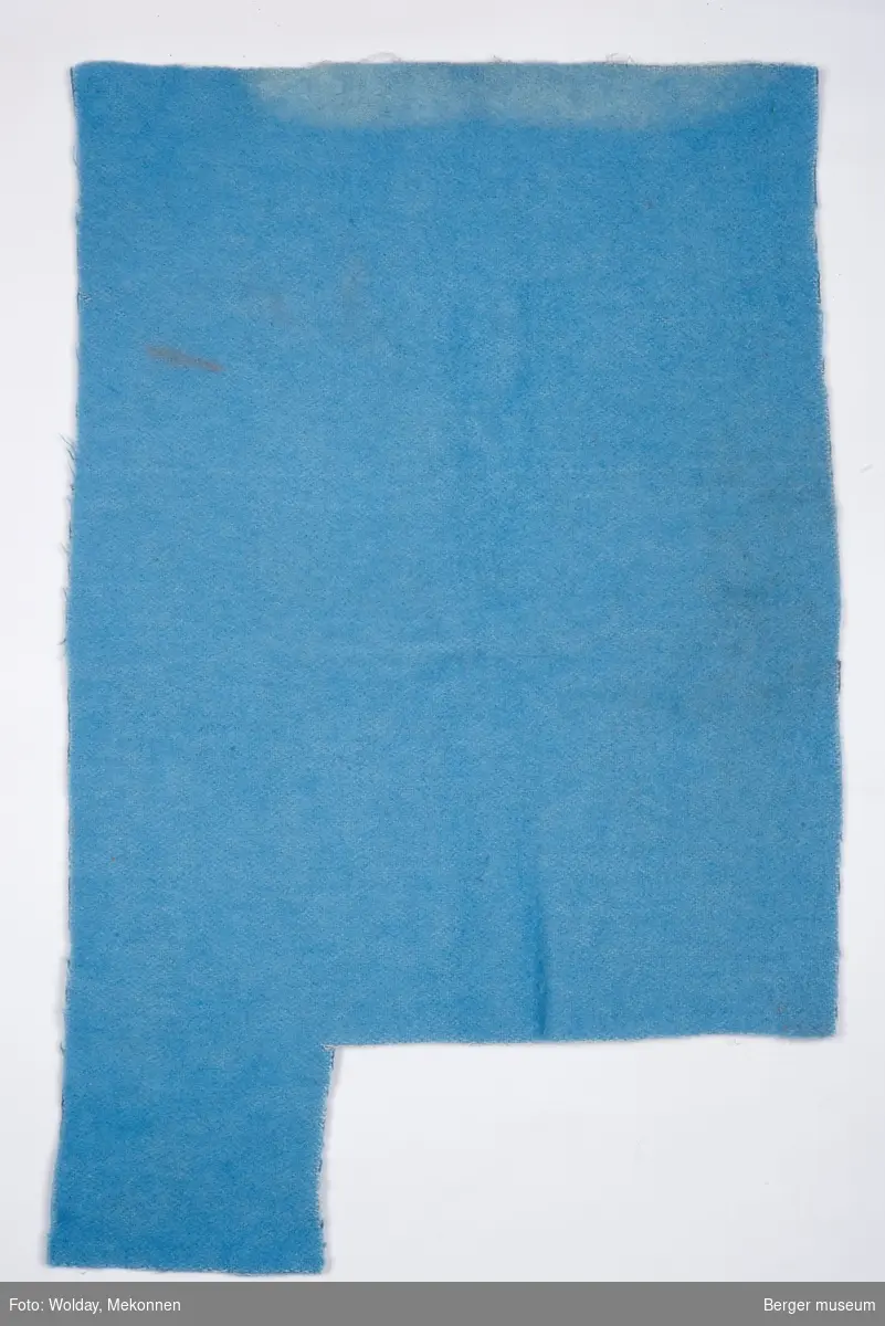 Rektangulært pleddstykke, med et avklippet stykke på den ene kortsiden, på 12 x 27 cm