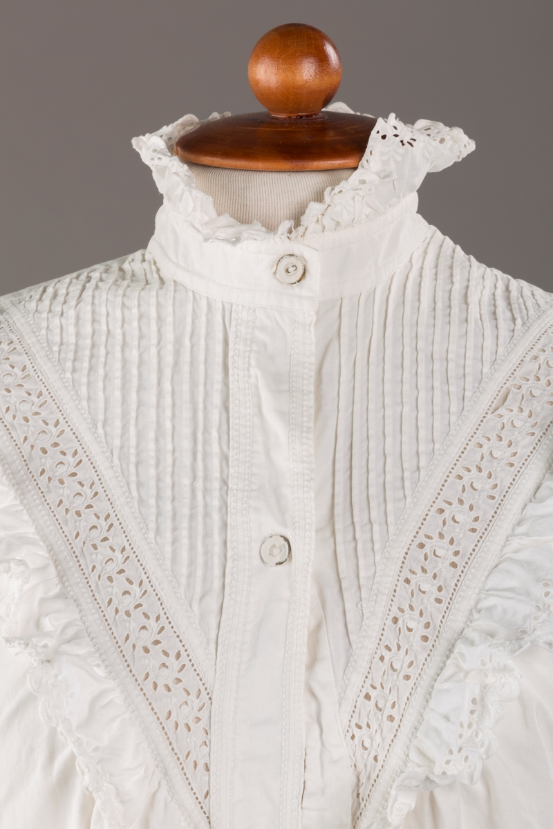 Form: Lange ermer, fotsid.

Blondekant og rysjer i halsåpning.
To knapper i metall kledd i tekstil. Mangler en knapp.