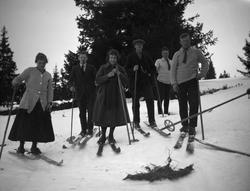 To kvinner i skjørt og 4 menn er ute på skitur.
