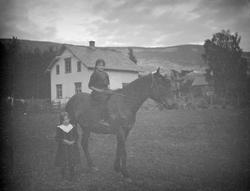 To jenter med hest. Hus i bakgrunn, mulig Ekrom.