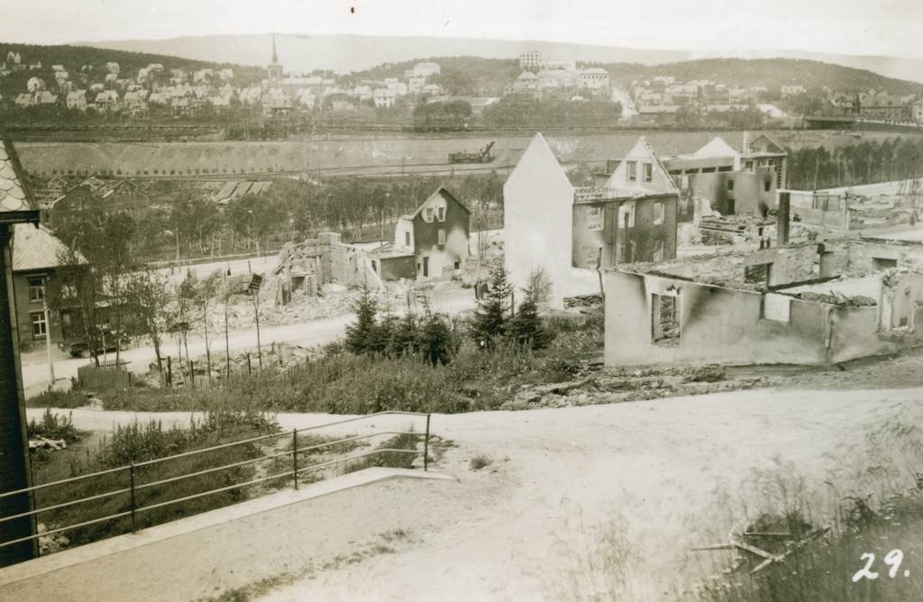 Ødeleggelser av bydelen Oskarsborg i Narvik i 1940. Hushjørnet helt til venstre er Håreksgt. 21. Huset bak bilen i Dronningensgt. er I.G. Kristensengården Dronningens gt. 19. Helt til høyre i Dr. gt. ser vi ruinen av Folkets Hus.