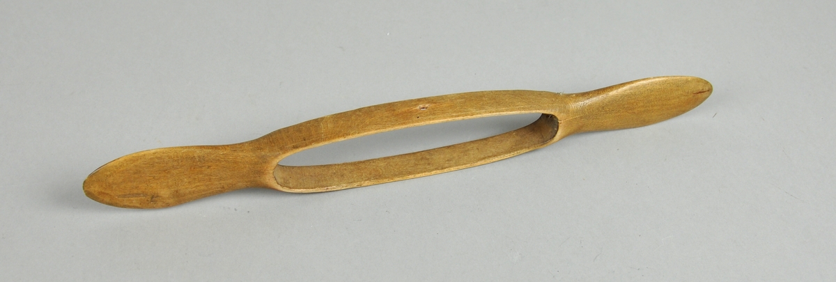 Vevskyttel av tre med lange håndtak på hver side. I midten er det skåret ut et hull, med plass til trådspolen.