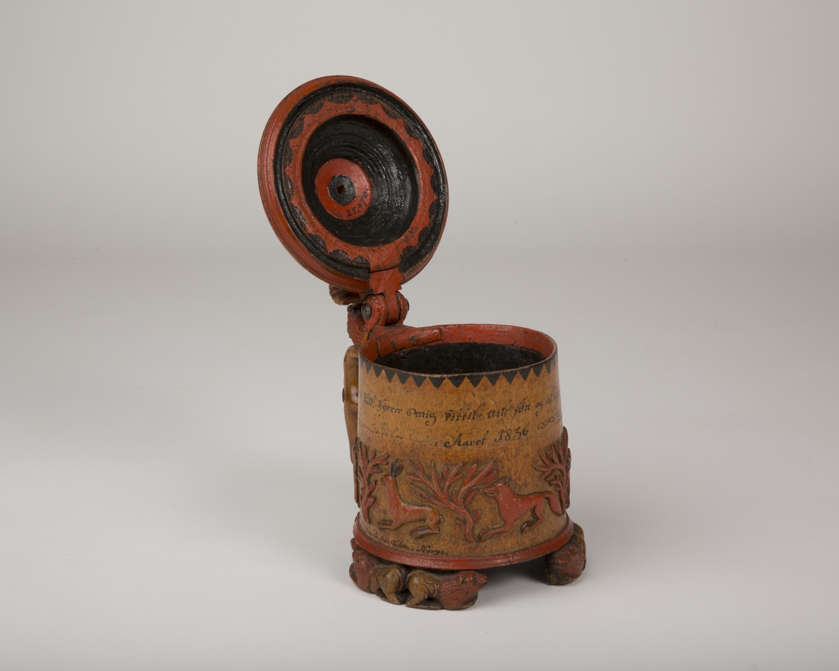 Dekorert med fortløpende billedfrise med dyr og trær på nederste del av korpus. Kannen har løveføtter og løvegjekk og bakkantine som håndtak. 