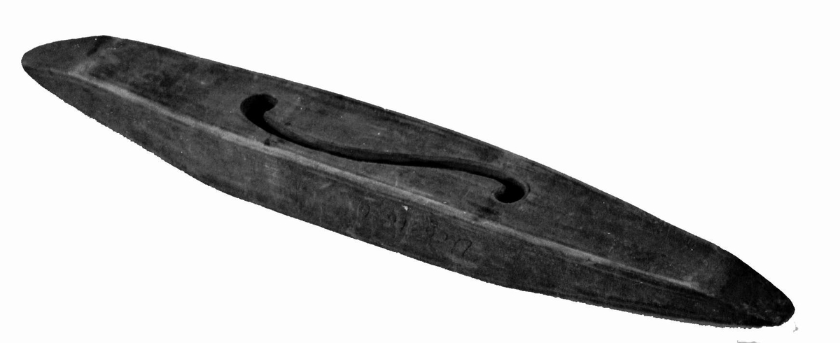 Avlang vevskyttel av tre med uthuling på midten, der hullet i bunnen er formet som en ranke.