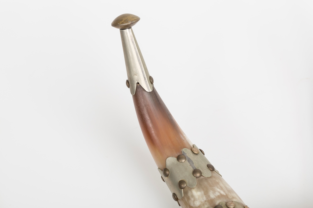 Knaggrekke antagelig håndlaget av kuhorn. 4 horn/kangger. Montert med "dekorative" beslag som er spikret og dekornaglet på hornene. Kledd med cordfløyelstoff på midtparti. To øyeskruer på toppen for feste til vegg.