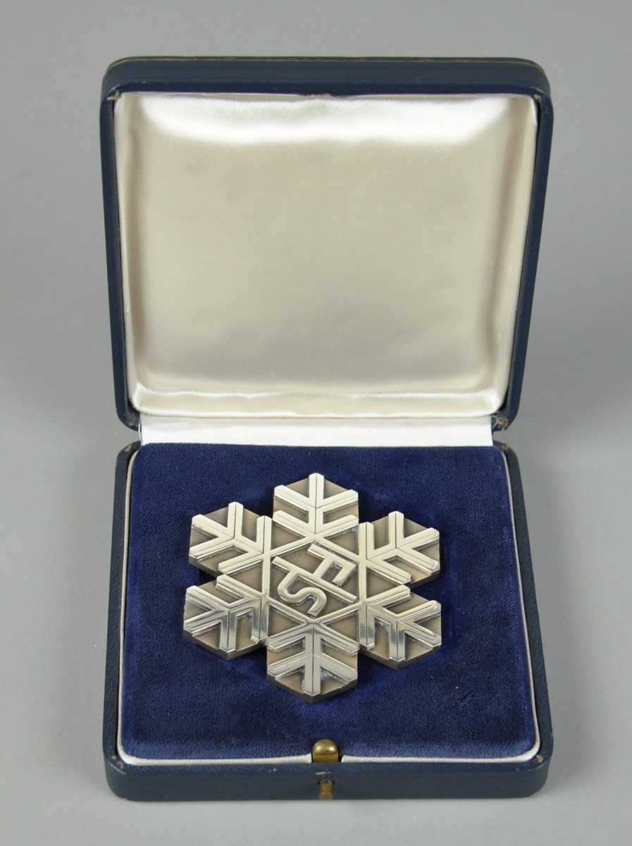 Sølvmedalje fra VM i langrenn i Squaw Valley 1960, formet og mønstret som et snøfnugg. 
Medaljen ligger i et blått etui merket FIS
