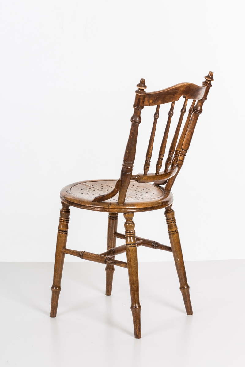 Stol i lakket treverk. Rundt stolsete med hullemønster. Rygg som er svakt buet med spiler og mønster. Dreide ben og spiler i rygg.