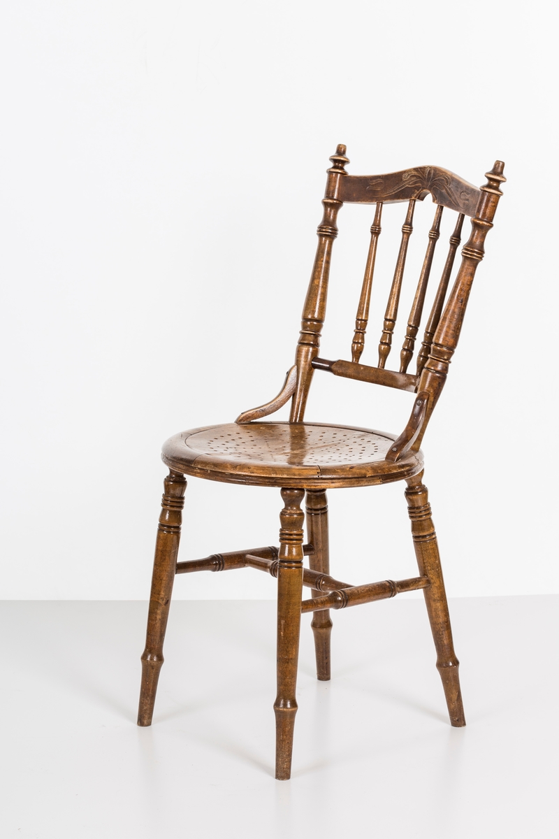 Stol i lakket treverk. Rundt stolsete med hullemønster. Rygg som er svakt buet med spiler og mønster. Dreide ben og spiler i rygg.