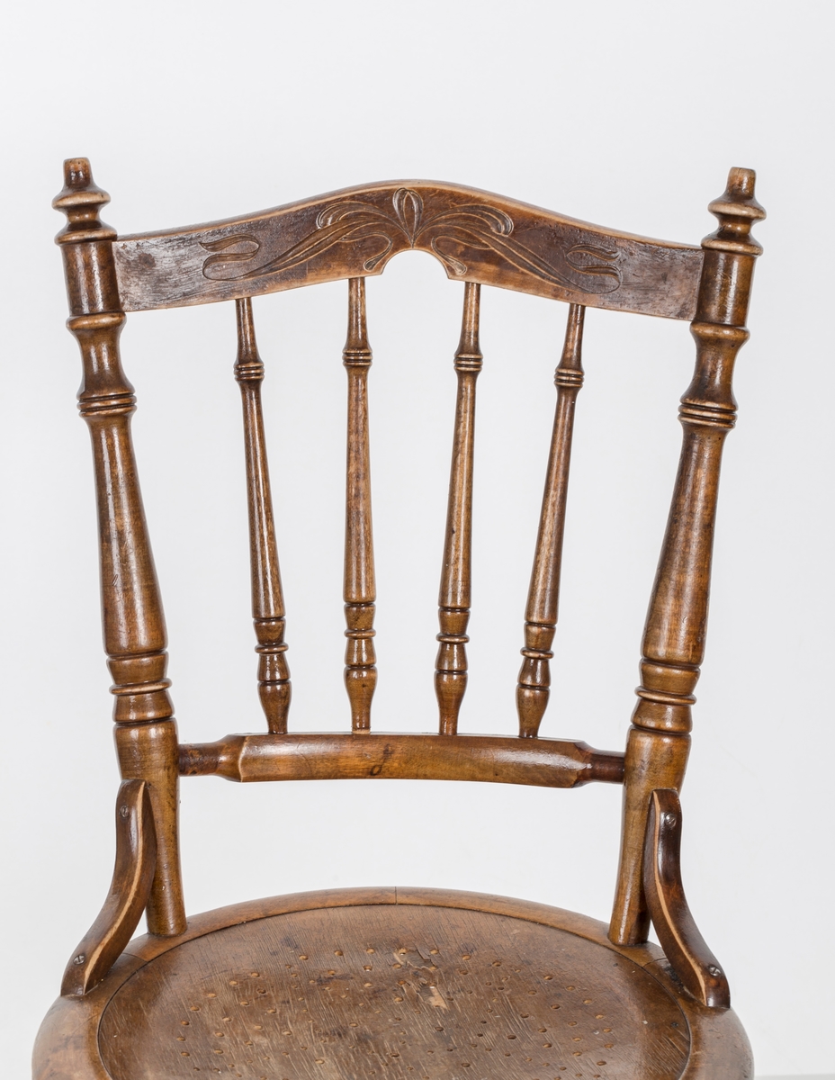 Stol i lakket treverk. Rundt stolsete med hullemønster. Rygg som er svakt buet med spiler og mønster. Dreide ben om spiler i rygg.