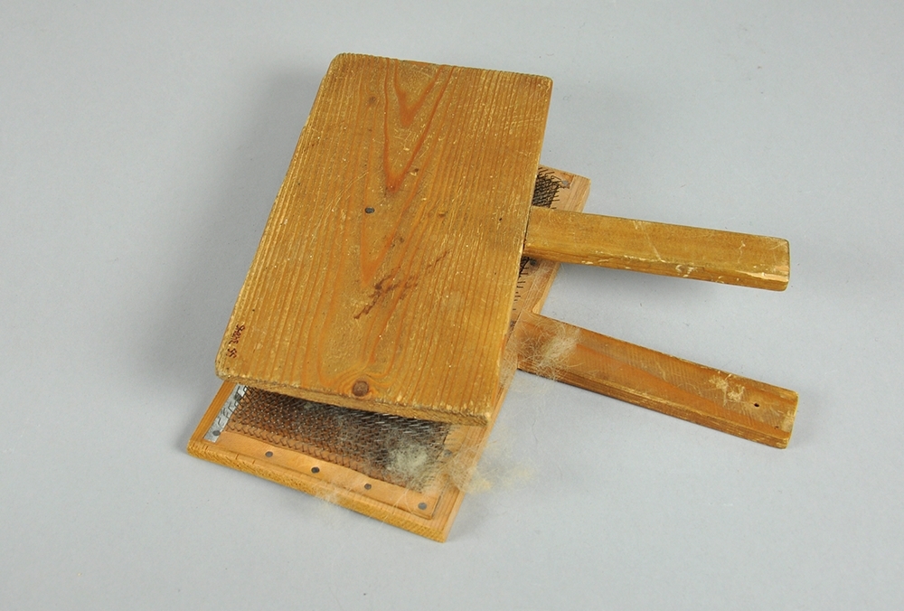 To treplater hvor innsiden av begge platene er dekket av en lærduk med tettsittende nåler. Begge treplatene har håndtak.