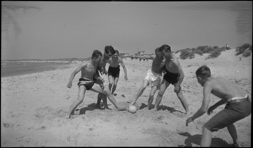 En stor vennegjeng i lystig lag på stranda på Sola. De har trommer og trekkspill og leker i vannet og på land med og uten ball. Sola strandhotell ligger i bakgrunnen. Tor Johannessen og Harald Bergsaker er på bilde nr. 14 og 18.