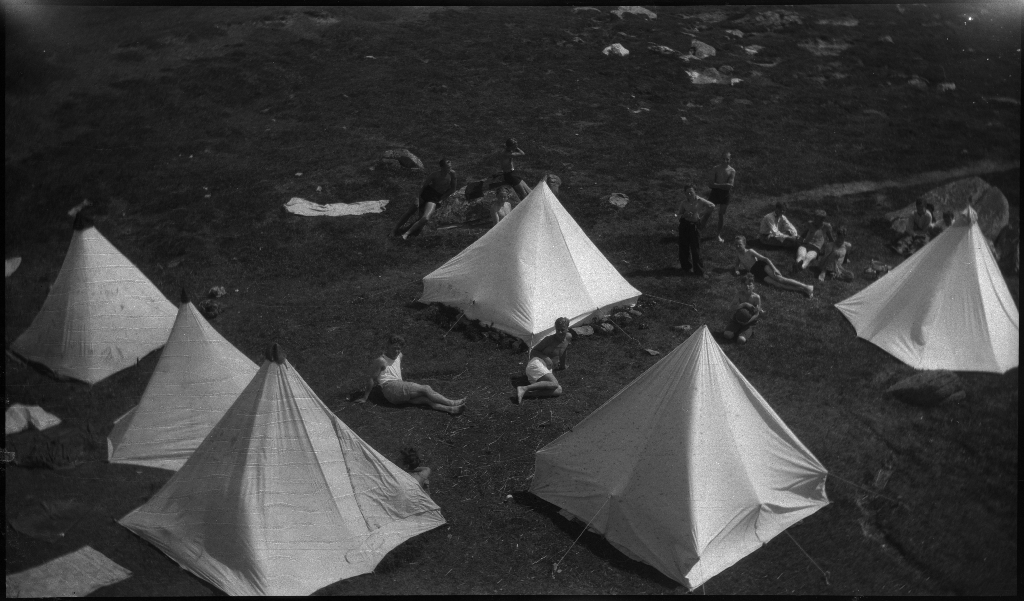 Barn og unge på og rundt stranda i Vigdelsvika. De fleste har satt opp telt, noen soler seg og noen bader. Den ene gutten på bilde nr. 6 holder et flytebelte.