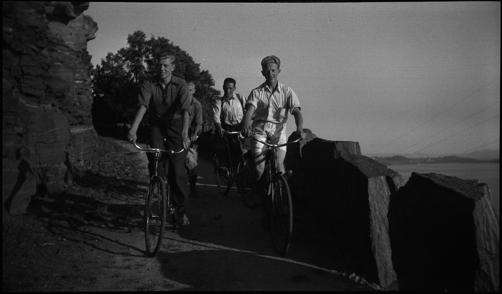Lindtner, Thaule, Arne og Tor Johannessen på tur på Rennesøy. Det er bilder fra en vik med et et naust, av landskapet og av guttegjengen som sykler. De er også på en topp med en varde.