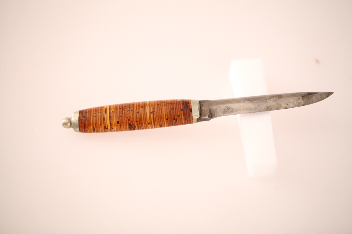 Kniv og slire hører ikke sammen. skaftet er laget av never, og slira er laget av nysølv. vanligvis hadde neverskaftkniver lærslire, og nysølvslirer hadde vanligvis ibenholdtskaft. Dekoren på slira er gravering og motivet er såkalte "Elstadkvister" slira er dermed høyest sannsynelig laget i Kolbu av en av Elstadkarene. Kniven har et fabrikkblad og er av ukjent opprinnelse.