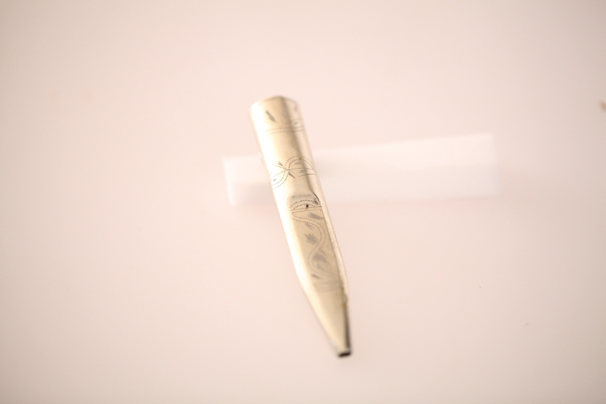 Kniv og slire hører ikke sammen. skaftet er laget av never, og slira er laget av nysølv. vanligvis hadde neverskaftkniver lærslire, og nysølvslirer hadde vanligvis ibenholdtskaft. Dekoren på slira er gravering og motivet er såkalte "Elstadkvister" slira er dermed høyest sannsynelig laget i Kolbu av en av Elstadkarene. Kniven har et fabrikkblad og er av ukjent opprinnelse.