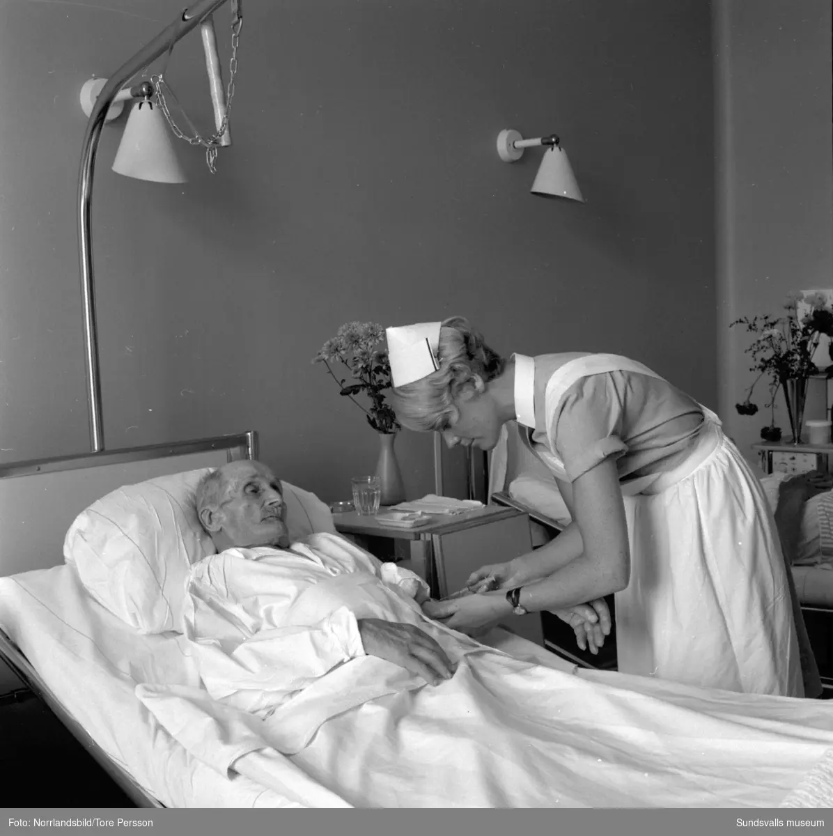 Sjuksköterskeskolan i Sundsvall. Två elever förbereder medicin till patienterna. En gammal man får en injektion.
