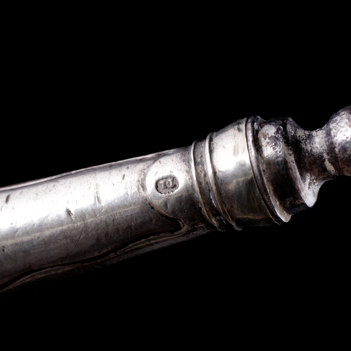 Bordsgaffel, tvåtenad i silver. 
Pistolmodell. Stämpel på skaftets nedre del: "I.W". (Kan möjligen vara: Jeremias Wallbom (1776-1807), Uddevalla).