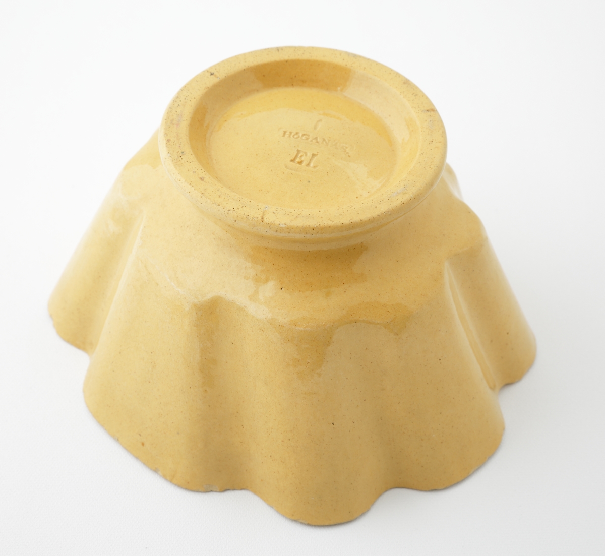 Aladåbform i keramik. 
Oval veckad form på fot, med inpressad dekor i form av druvklase i botten. Honungsgul glasyr.