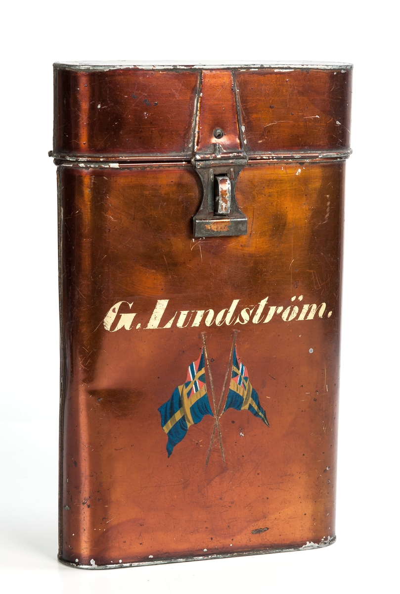 Brevlåda, kopparmålad plåt. Brevlåda m. lock. På framsidan texten, G. Lundström (i gult). Under namnet två korslagda unionsflaggor.