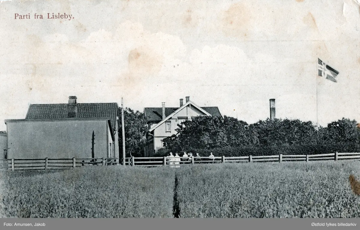 Postkort med parti fra Lisleby.
Postkort med motiv fra Lisleby, landhandel, og bakeri, ca. 1905-10 mot Selbak fergested. Aasta Gjøby arbdeidet der. Bygningen brant engang før 1920.
I dag ligger NorBetong Ferdigbetong på stedet, dagens adresse er Dr. Opsandsvei 33.
Gruppe med 8 personer står langs gjerdet.

Huset var et av husene som gikk med i brannen på bordtomten til Lisleby bruket 10 mai 1915. Der alle bordhusene og 11 beboelseshus gikk med i brannen. Jacob Amundsen tok etter det over Fredrikstad Fargehandel i Baggaden 2, som Farmanns gate het den gangen. (Johreid, info 2018).