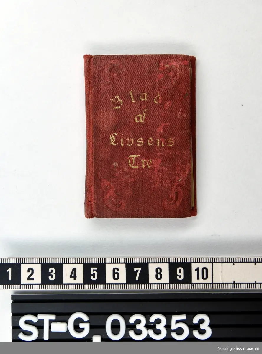 Huspostill: liten bok (miniatyr) innbundet i rød tekstil med dekorativt reliefftrykk og boktittel i gull. Boken inneholder et bibelvers for hver av årets dager i gotisk skrift.