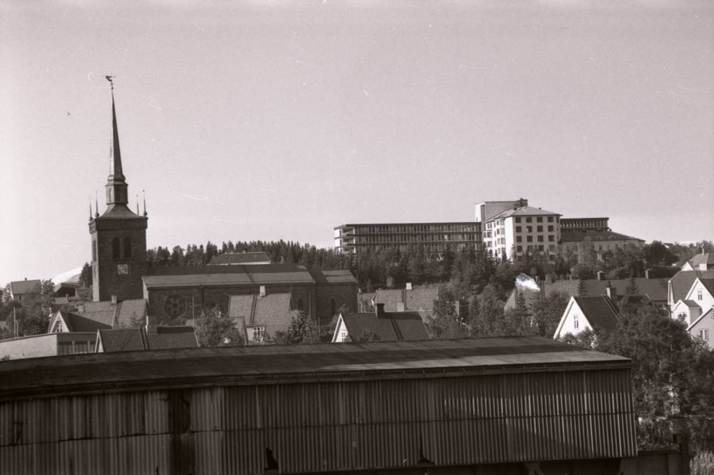 Narvik kirke. Narvik Sykehus.
Bolaget i retning nord. Det er mest trolig vegg og taket til lossestasjonen som sto på banegården (ca rett ovenfor Sentralstasjonen) og ble fjernet etterat nye lossestasjonen ble tatt i bruk ca 1974-75. Her kunne det losses 4 tog samtidig.